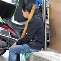 Middle-aged worker resting on a ledge holding a thick bamboo carrying pole beside a street in Chongqing