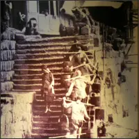 Historical photo at the Three Gorges Museum showing laborers carrying heavy loads on shoulder poles up staircases