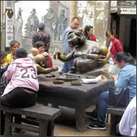 Visitors sitting together at a table with metal sculptures depicting daily life, including a mother with children