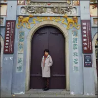 A woman stands beneath an ornate stone temple portal decorated with colourful Chinese characters and painted details.
