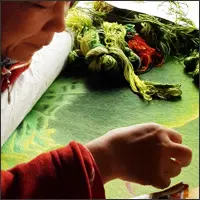 Close-up of an artisan guiding a needle through fabric stretched tightly across an embroidery frame.