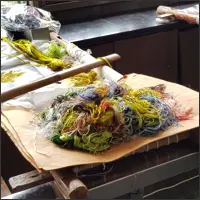 Fine strands of silk thread in green, yellow, red, purple and other colours are arranged beside an embroidery frame.