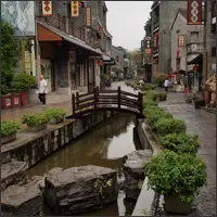 Narrow canal with stone bridges and traditional buildings in Lingnan Impressions Park.