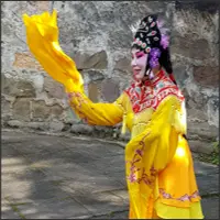 Performer in bright yellow traditional Chinese opera costume posing outdoors.