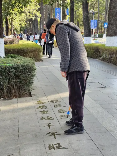 Man practicing traditional Chinese water calligraphy on a sidewalk, writing large characters with water.