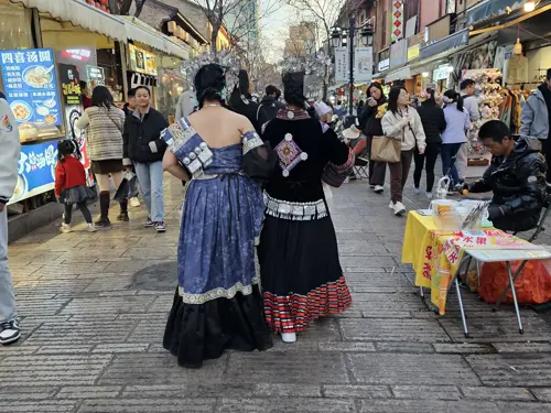Two women walking along a pedestrian street in China wearing colorful ethnic-style costumes.