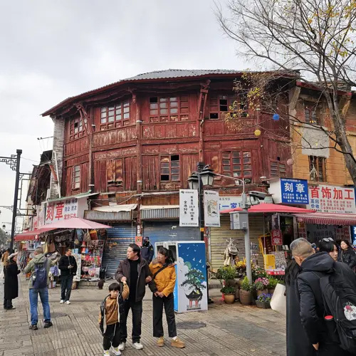 Curved two-story wooden merchant house in Kunming’s old town, with traditional eaves and weathered facade facing a street market area.