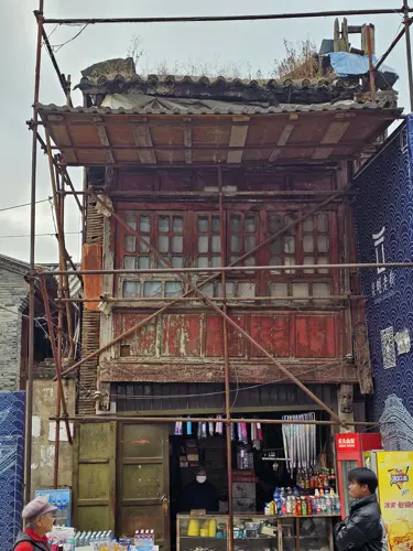 Old wooden house in Kunming supported by exterior scaffolding, the structure visibly aged and partially deteriorated.