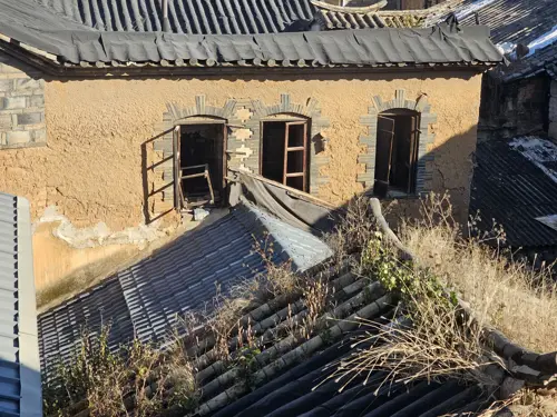 View from above of a block of abandoned old houses in Kunming’s old town, with tiled roofs, crumbling walls, and patches of overgrown vegetation.