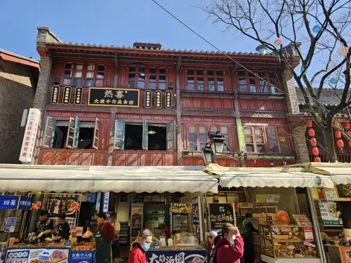 Recently constructed building in traditional Chinese architectural style, with wooden details and small storefronts displaying goods along the street.