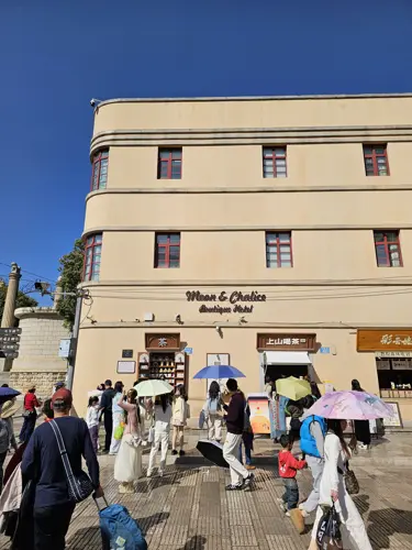 Flat side view of Kunming’s wine cup building, standing above a busy public square on a bright day with many people around.